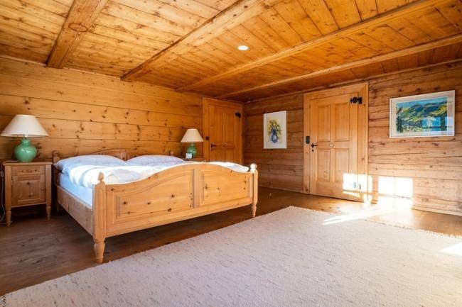 Helles Schlafzimmer mit Holzboden und -wänden, einem großen Bett und einem Teppich, der den Raum gemütlich macht.