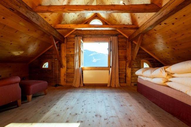 Geräumiges Dachgeschoss mit Holzbalken, einem Bett und einem großen Fenster mit Bergblick.