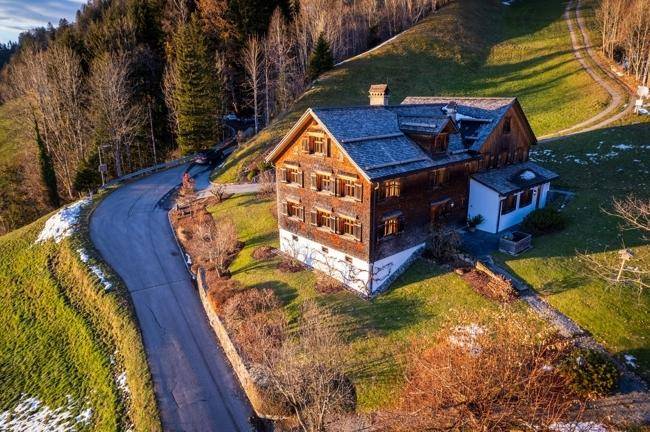 Luftaufnahme des traditionellen Holzhauses, eingebettet in die grüne Hügellandschaft mit kurviger Zufahrt.