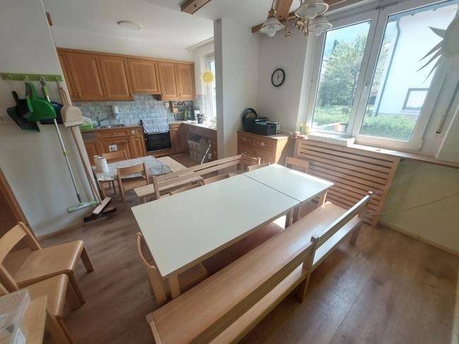 Küche mit Holzschränken, großem Esstisch und viel Tageslicht durch die Fenster.