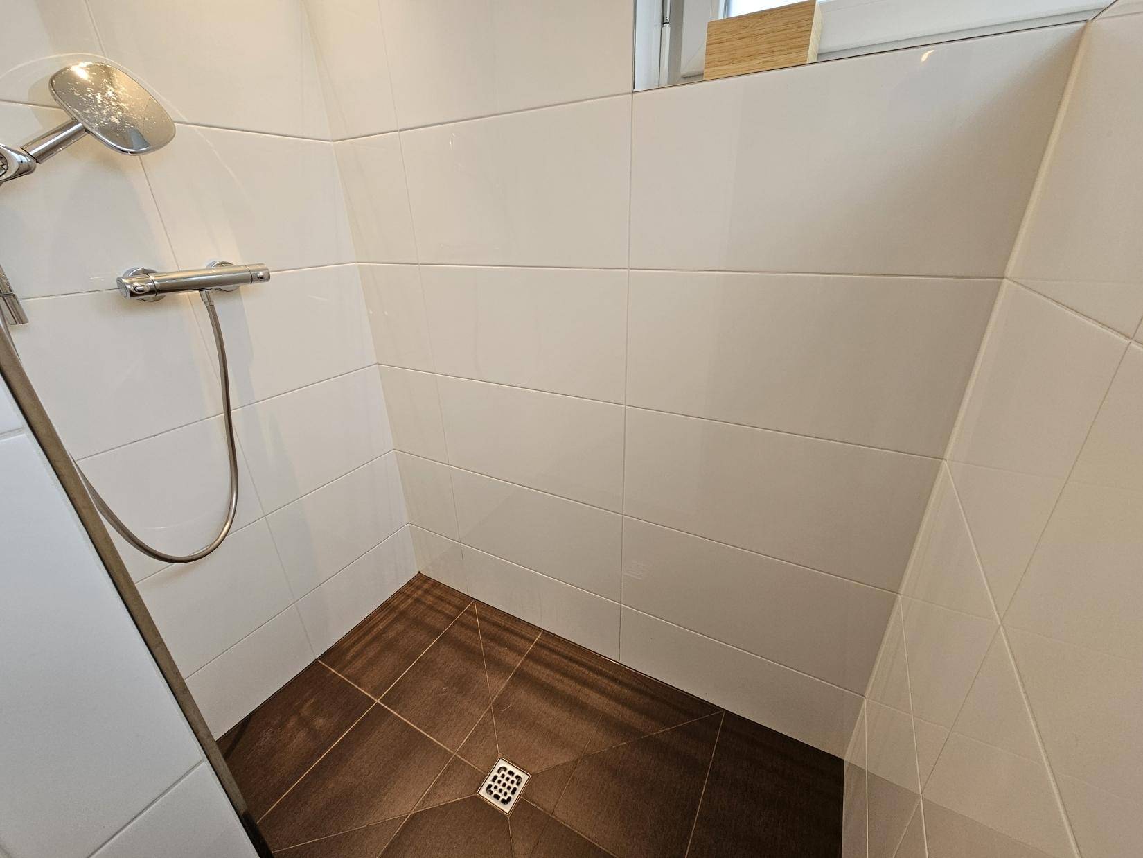 Ebenerdige Dusche mit braunen Bodenfliesen und weißen Wandfliesen.