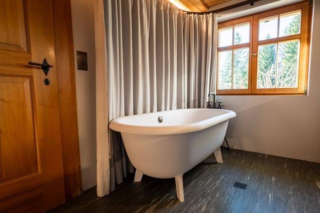 Elegantes Badezimmer mit freistehender Badewanne und einem Fenster, das einen schönen Blick ins Grüne bietet.
