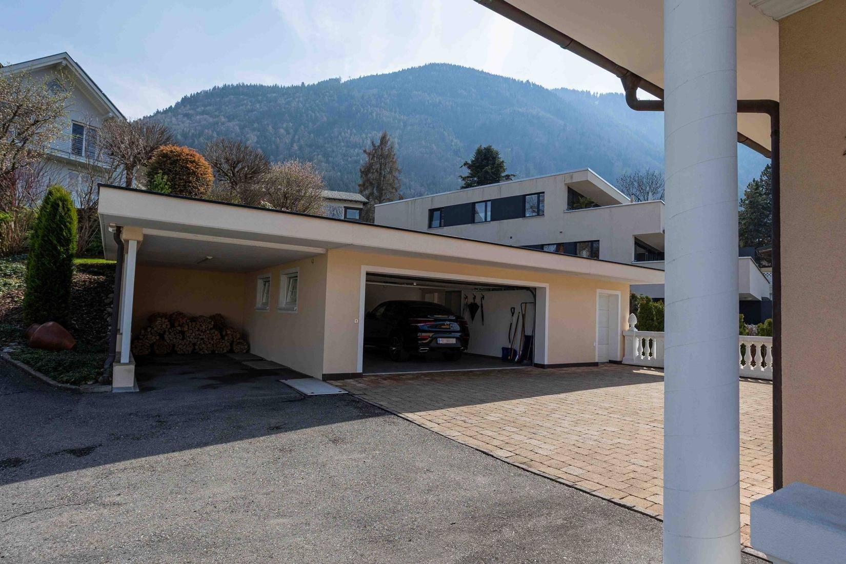 Ansicht der Doppelgarage und des Carports mit der Villa im Hintergrund und Bergblick.