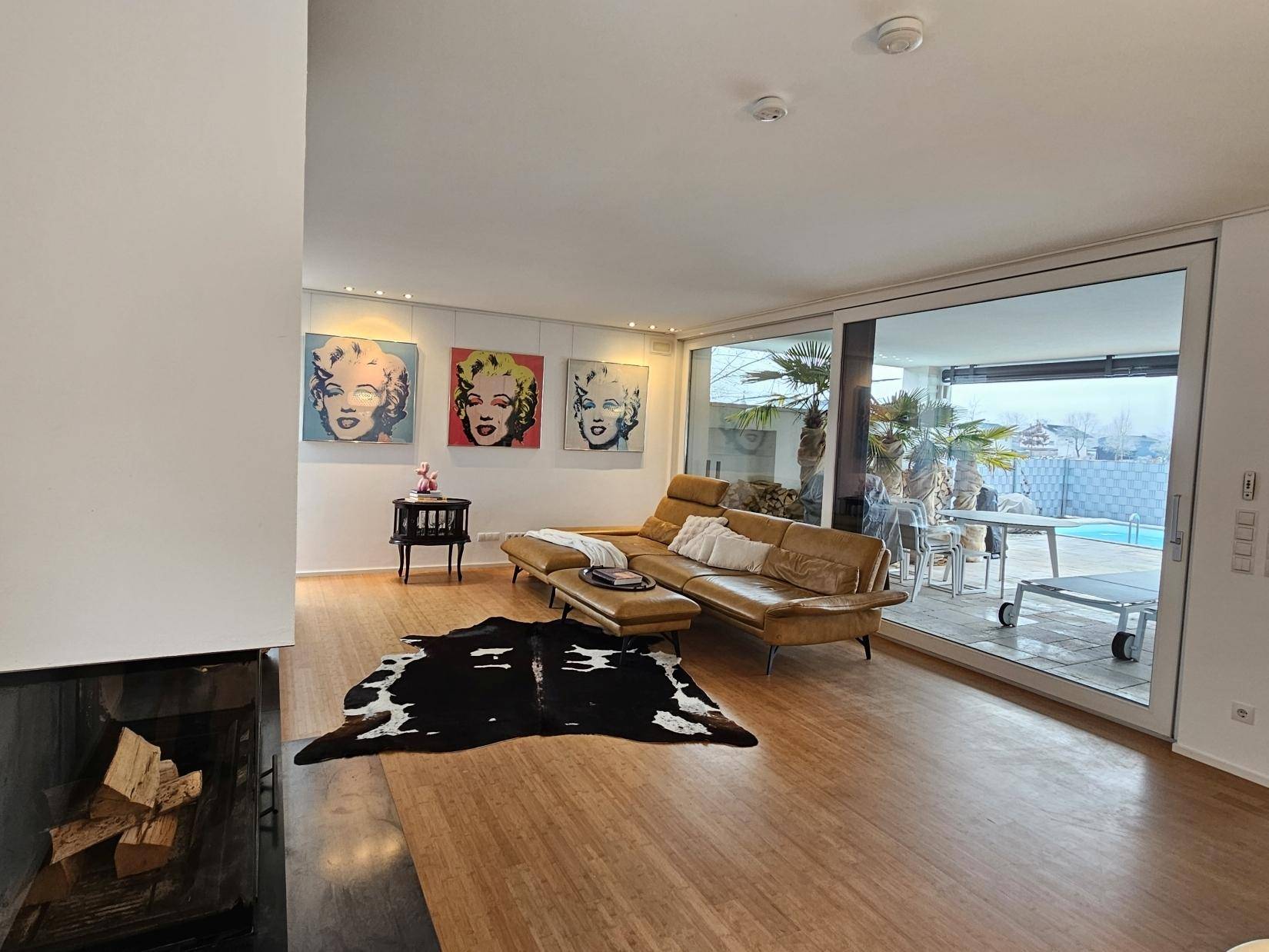 Gemütliches Wohnzimmer mit Kamin und großen Glasfronten zum Außenbereich mit Pool.