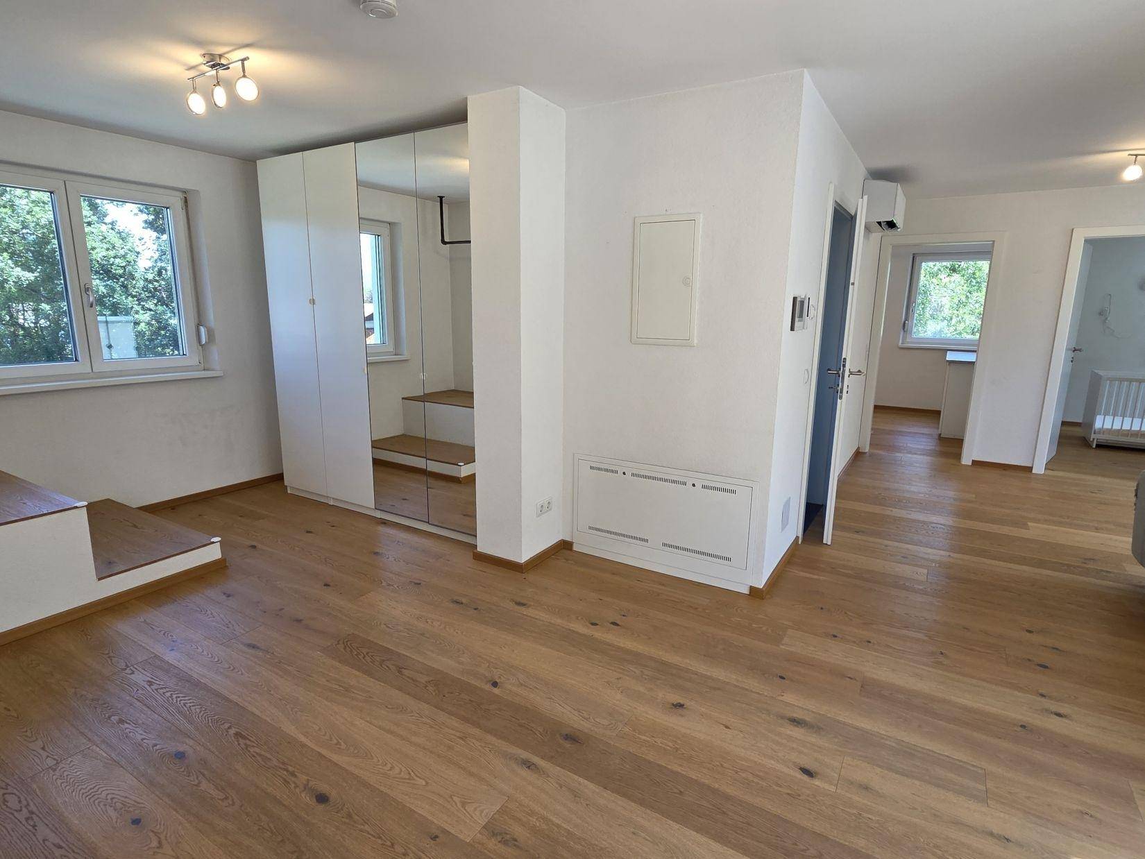 Heller Wohnbereich mit Eichenparkett, großen Fenstern und integriertem Spiegelschrank.