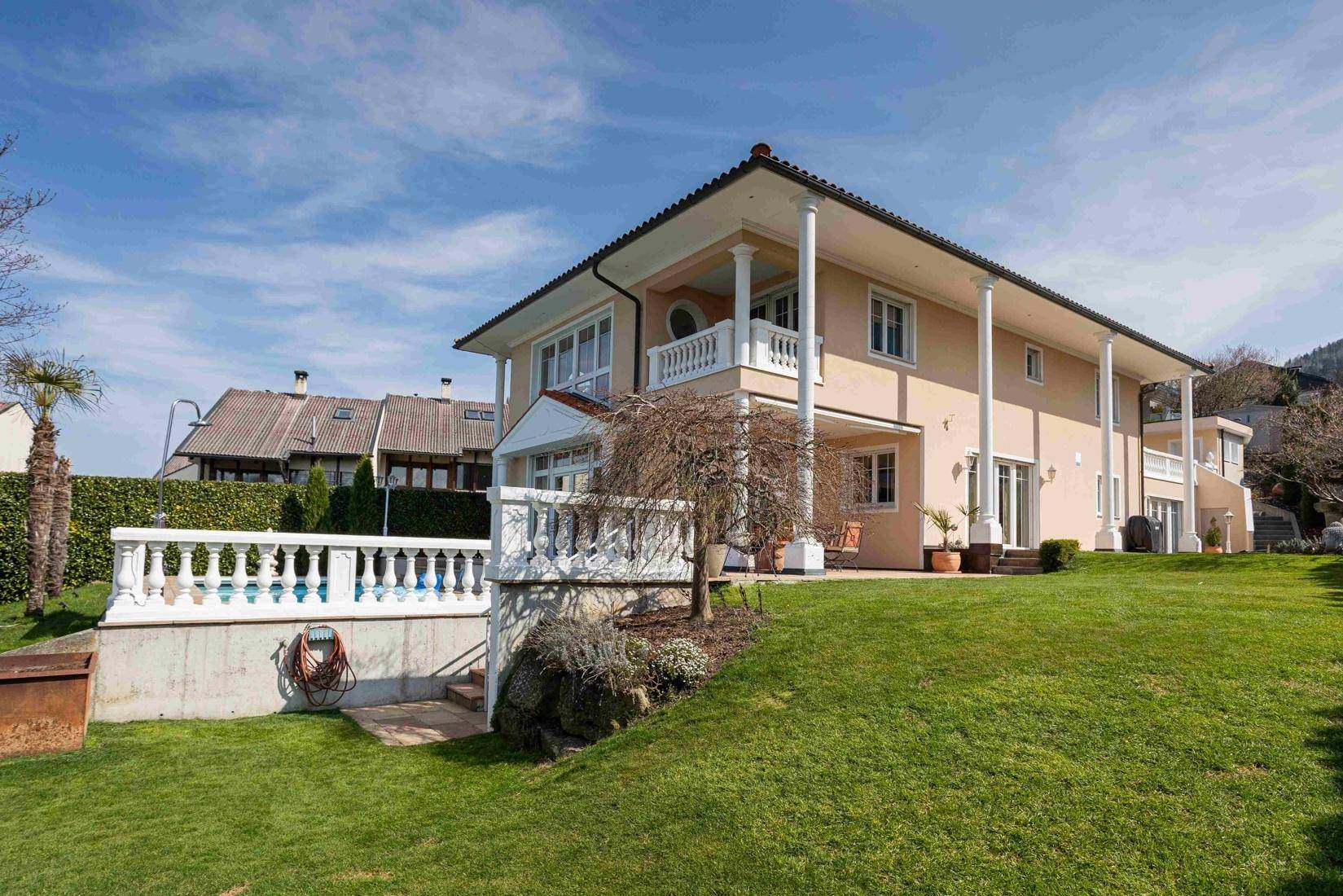 Seitliche Ansicht der Villa mit weitläufigem Garten und Poolbereich im Hintergrund.