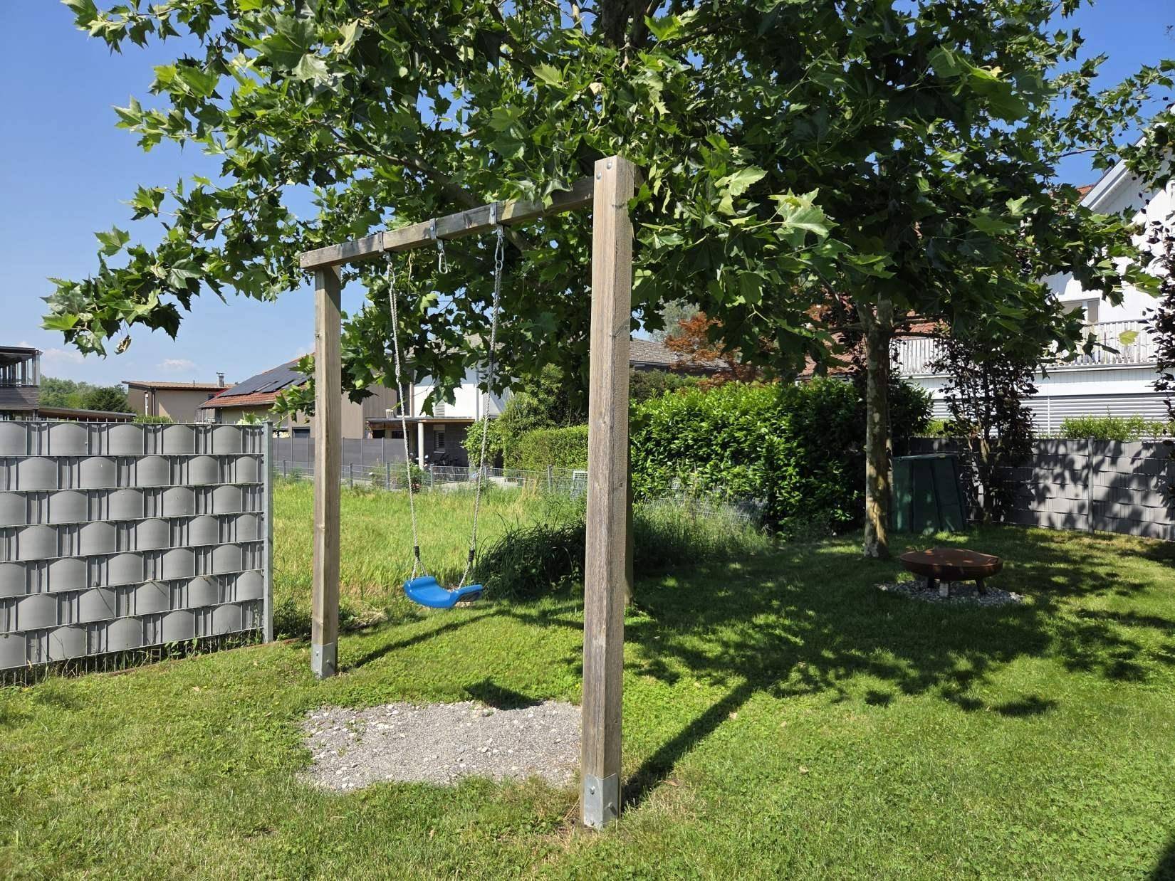Grüner Gartenbereich mit Schaukel und Feuerstelle, ideal für Kinder und entspannte Abende.