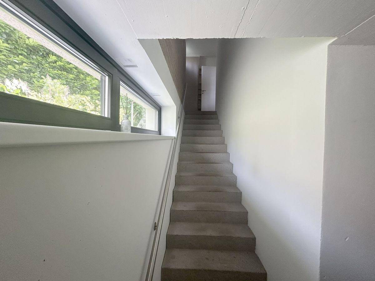 Heller Treppenaufgang mit Betonstufen und einem langen Fenster, das viel Tageslicht hereinlässt.