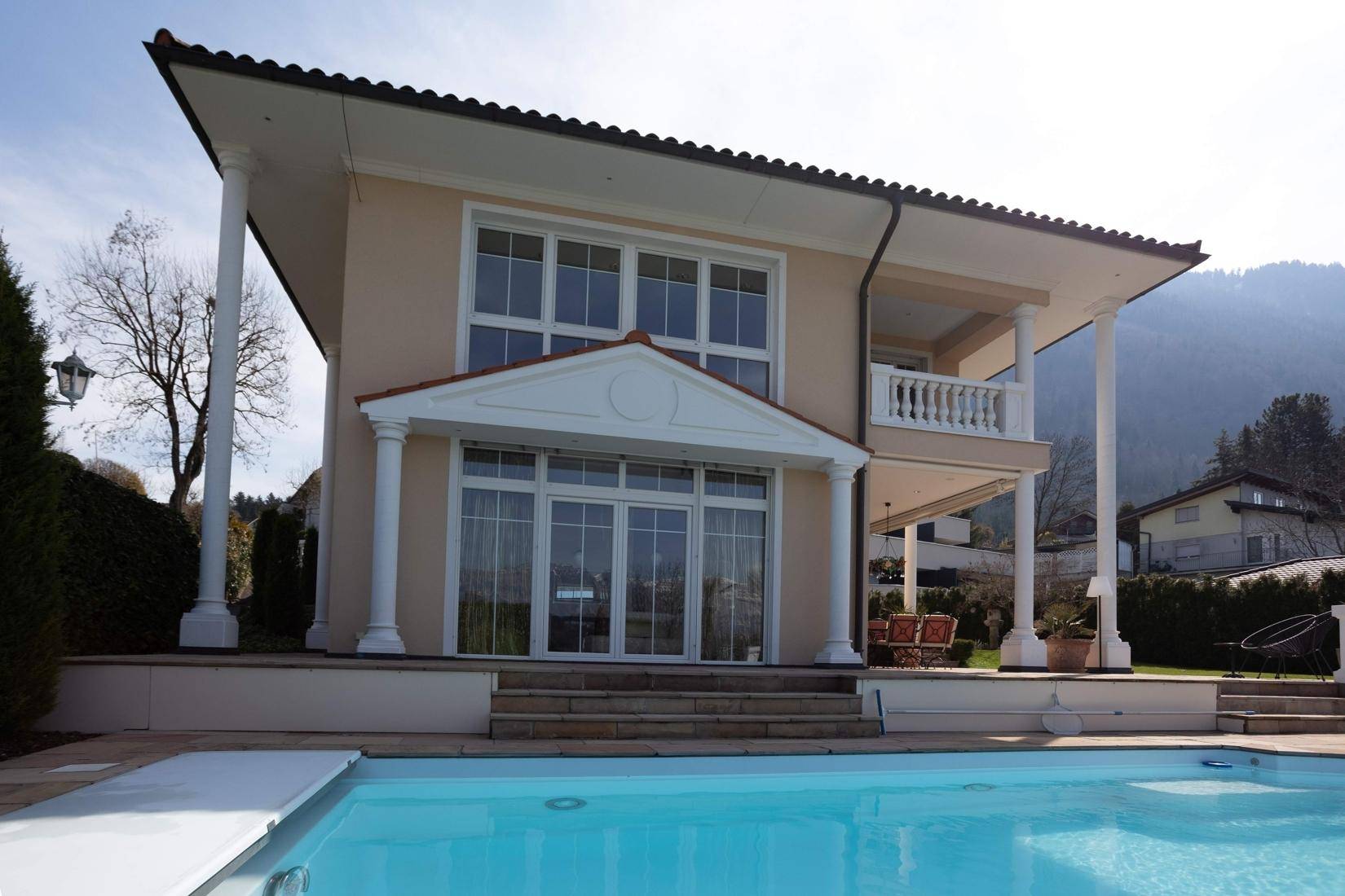 Rückansicht der Villa mit großem Pool und Terrasse unter blauem Himmel.