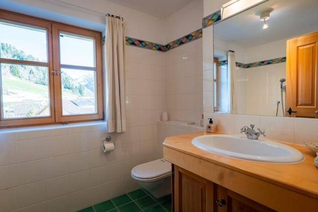 Badezimmer mit Holzwaschtisch, WC und einem Fenster, das einen weiten Blick auf die Berge bietet.