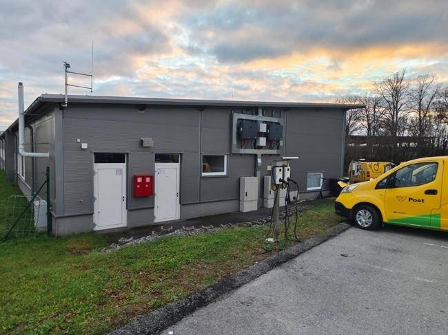 Seitenansicht des Gebäudes mit Türen, externen Installationen und Ladestationen für Fahrzeuge.