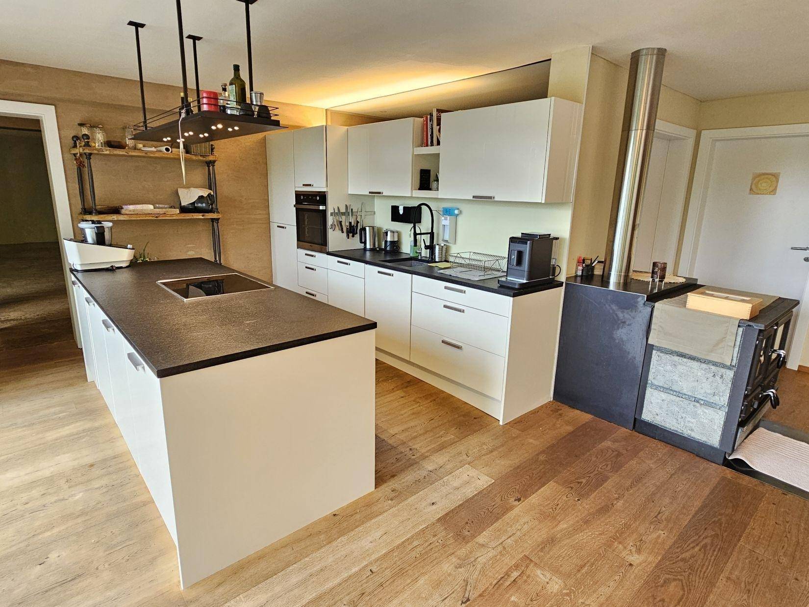 Moderne Küche mit weißer Einbauküche, Kochinsel und dunkler Arbeitsplatte, integriertem Holzofen.