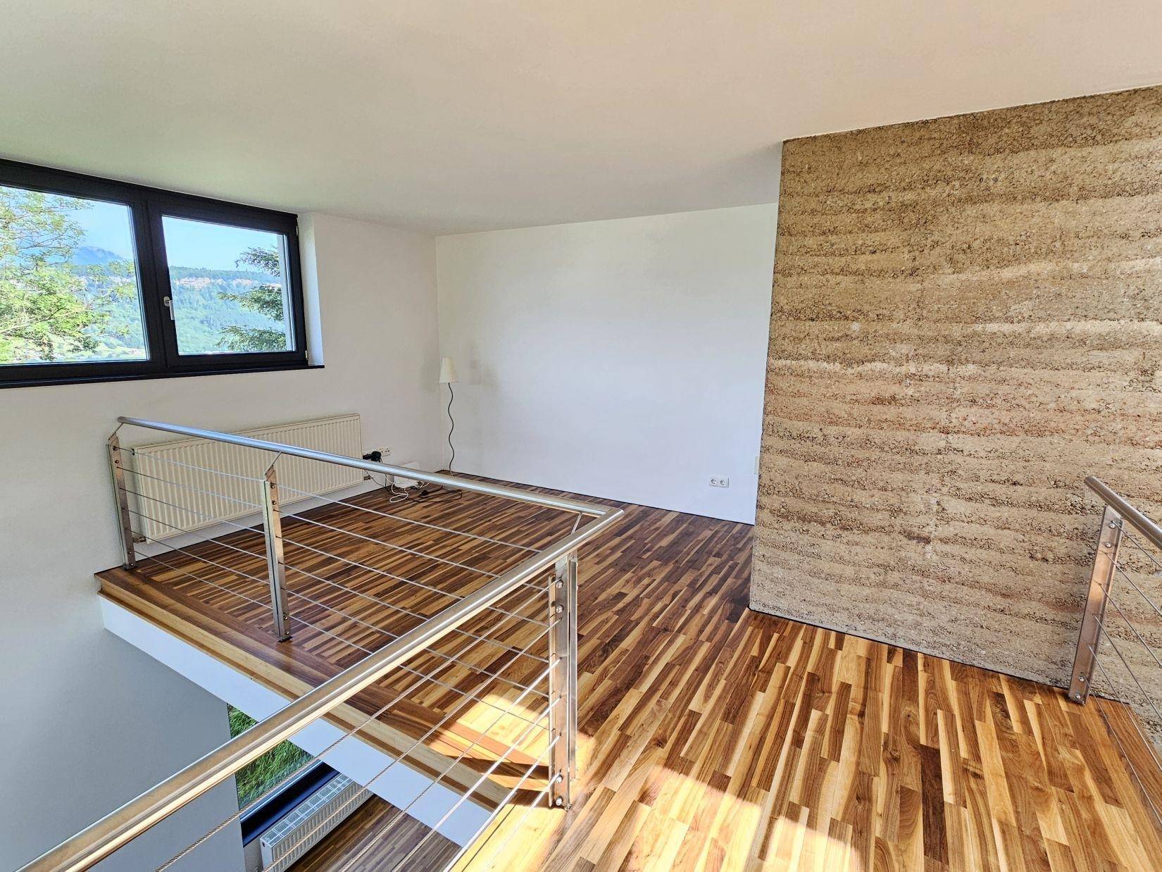 Offener Galeriebereich mit Holzparkettboden und einer markanten Wand aus gestampftem Lehm.