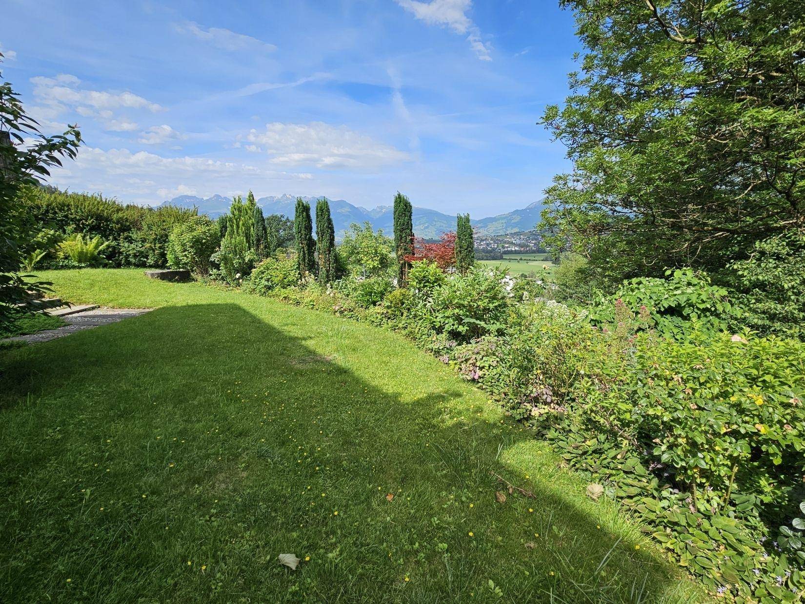 Weitläufiger Garten mit großer Rasenfläche und Panoramablick auf die umliegende Landschaft und Berge.