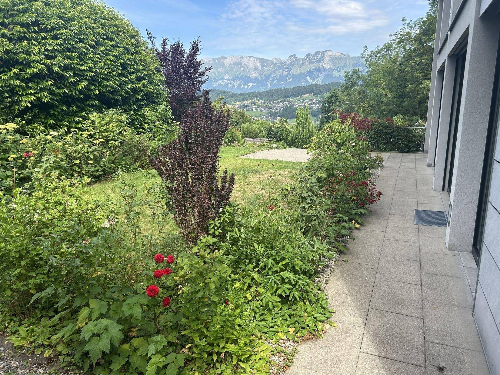 Gepflegter Gartenbereich mit Rasenfläche, Blumenbeeten und einem beeindruckenden Bergblick.