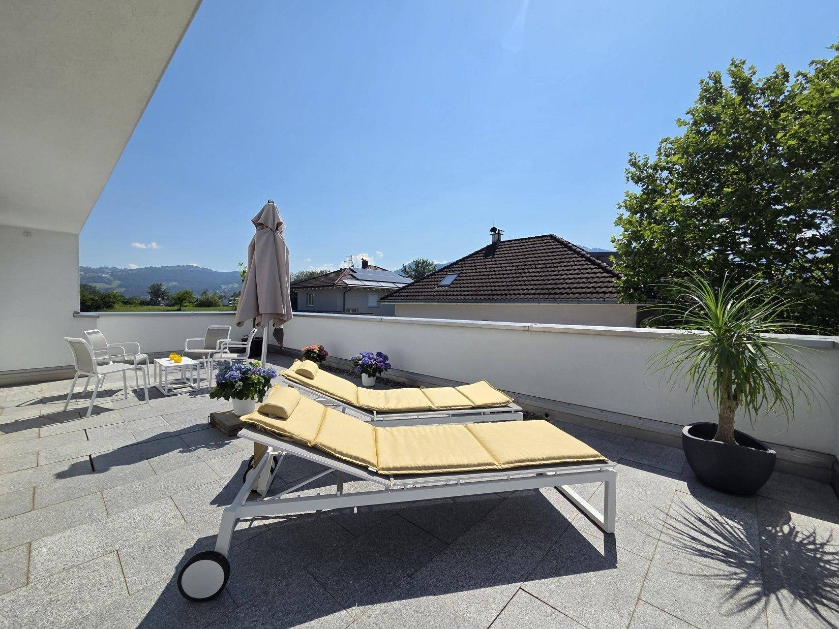 Großzügige Dachterrasse mit Sonnenliegen und Schirm, ideal zum Entspannen mit weitem Blick.