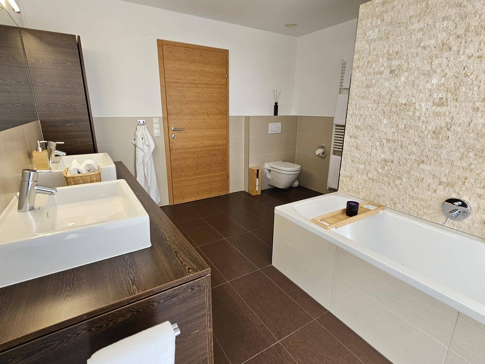 Helles Badezimmer mit Badewanne, Doppelwaschbecken und modernen Fliesen an Wand und Boden.