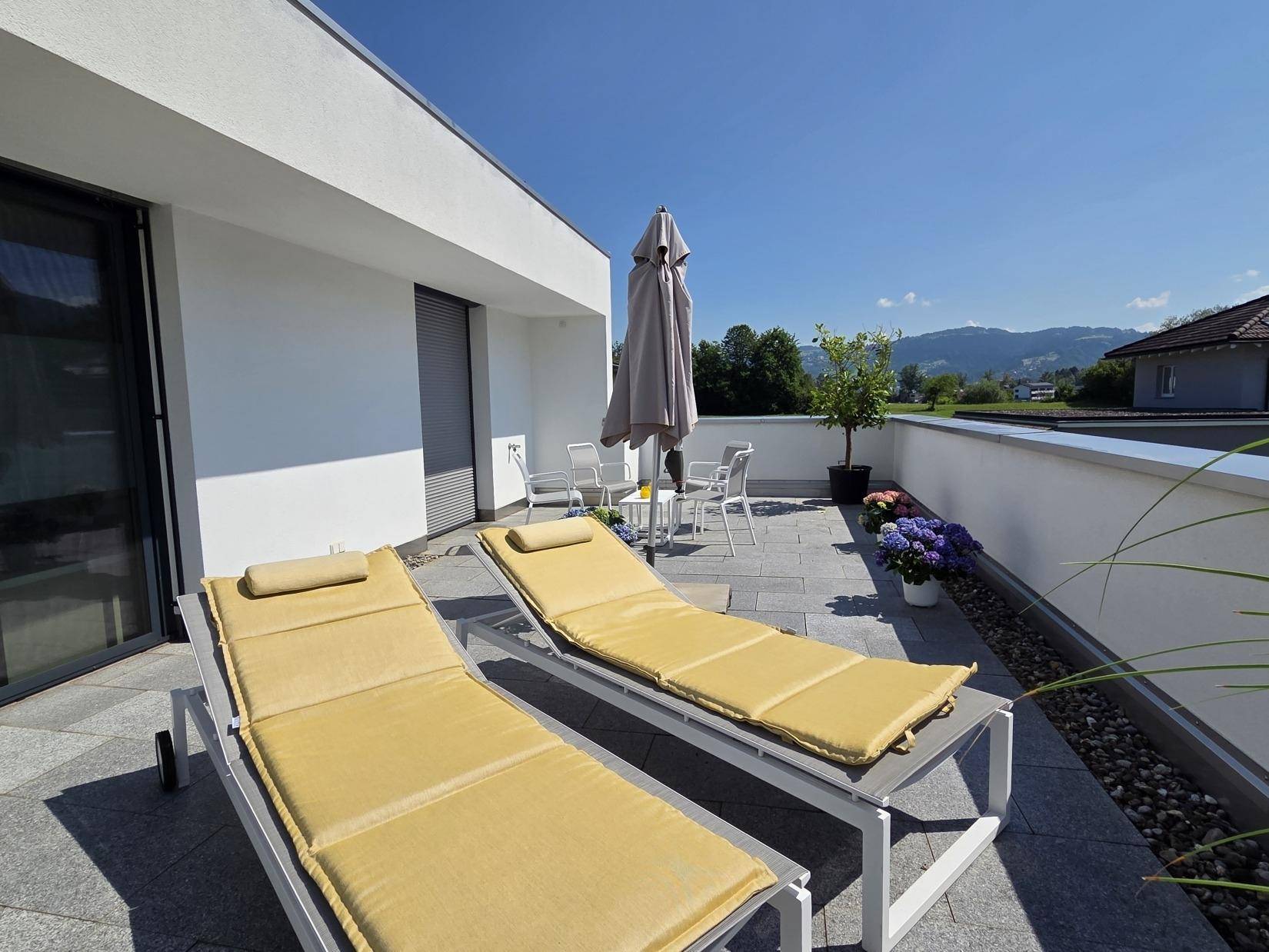 Helle Dachterrasse mit bequemen Sonnenliegen und Blick auf die umliegende Landschaft.