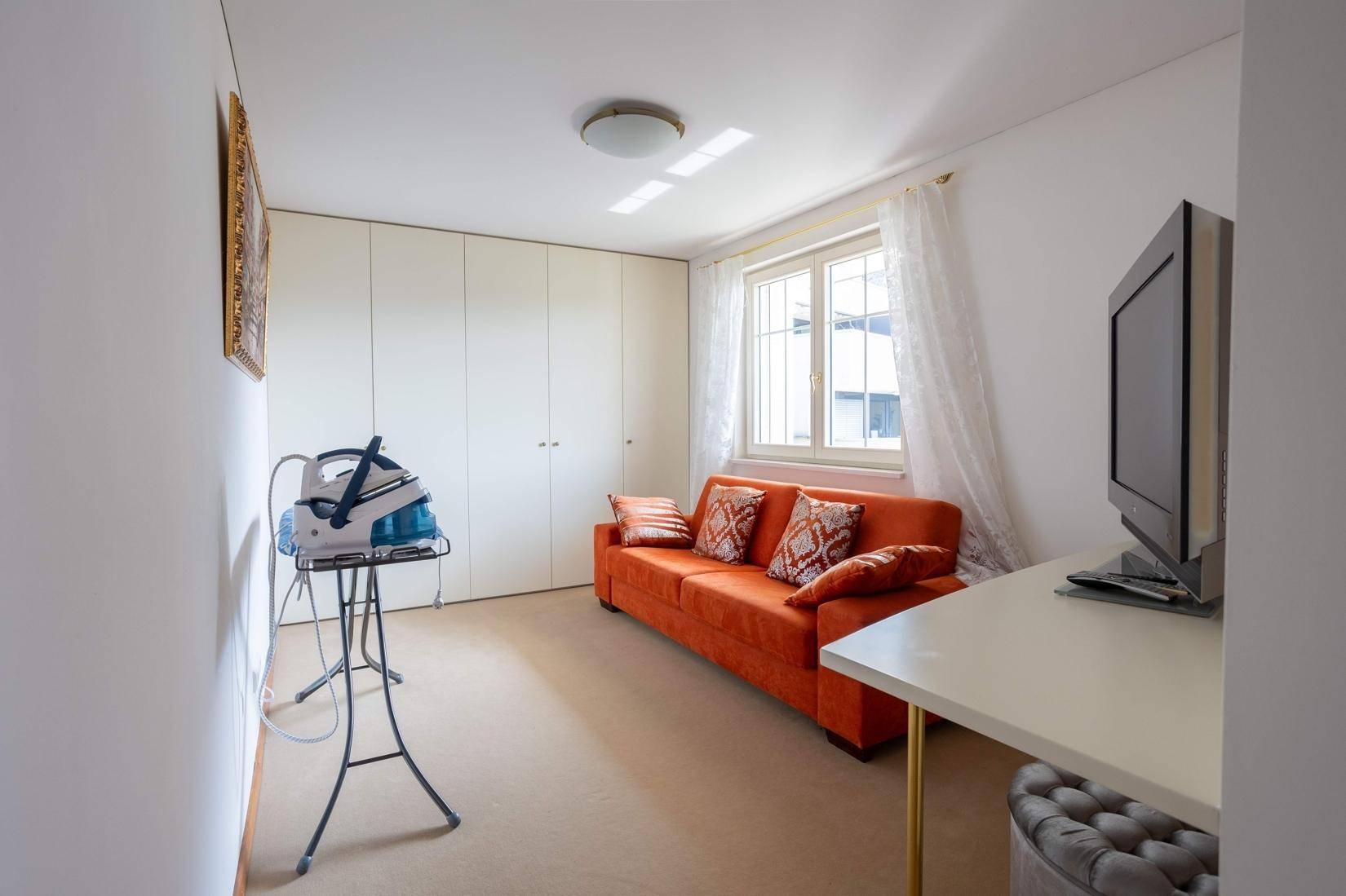 Vielseitiger Raum mit Schränken, Sofa und Fenster, nutzbar als Gäste- oder Bügelzimmer.