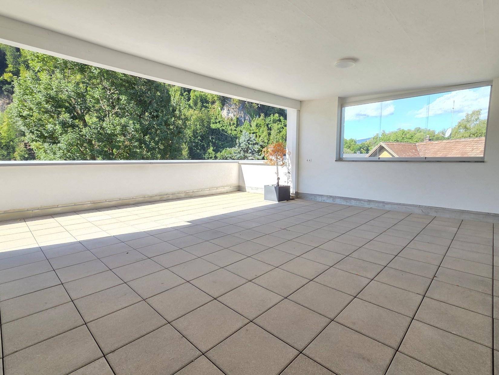 Große, überdachte Terrasse mit Fliesenboden und weitem Blick auf die bewaldeten Berge.