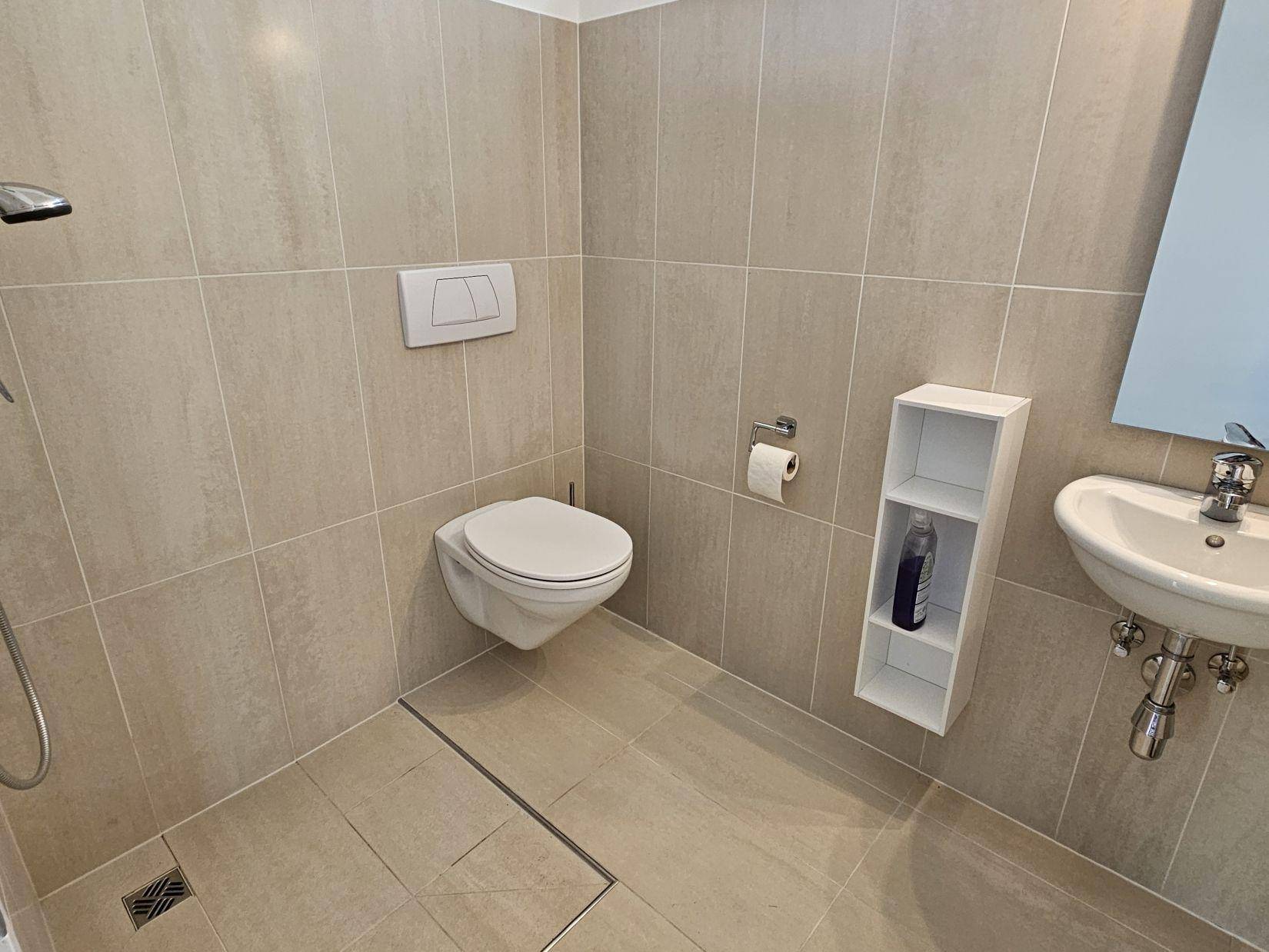 Modernes Badezimmer mit beigefarbenen Fliesen, wandhängendem WC und ebenerdiger Dusche.