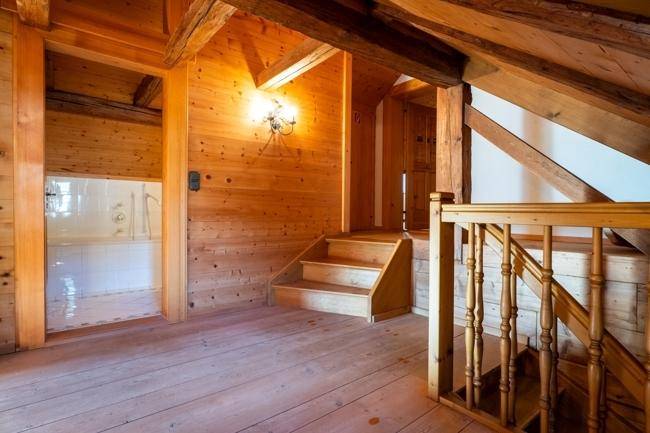 Dachgeschoss mit sichtbaren Holzbalken und einer Holztreppe, die zu einem weiteren Bereich führt.
