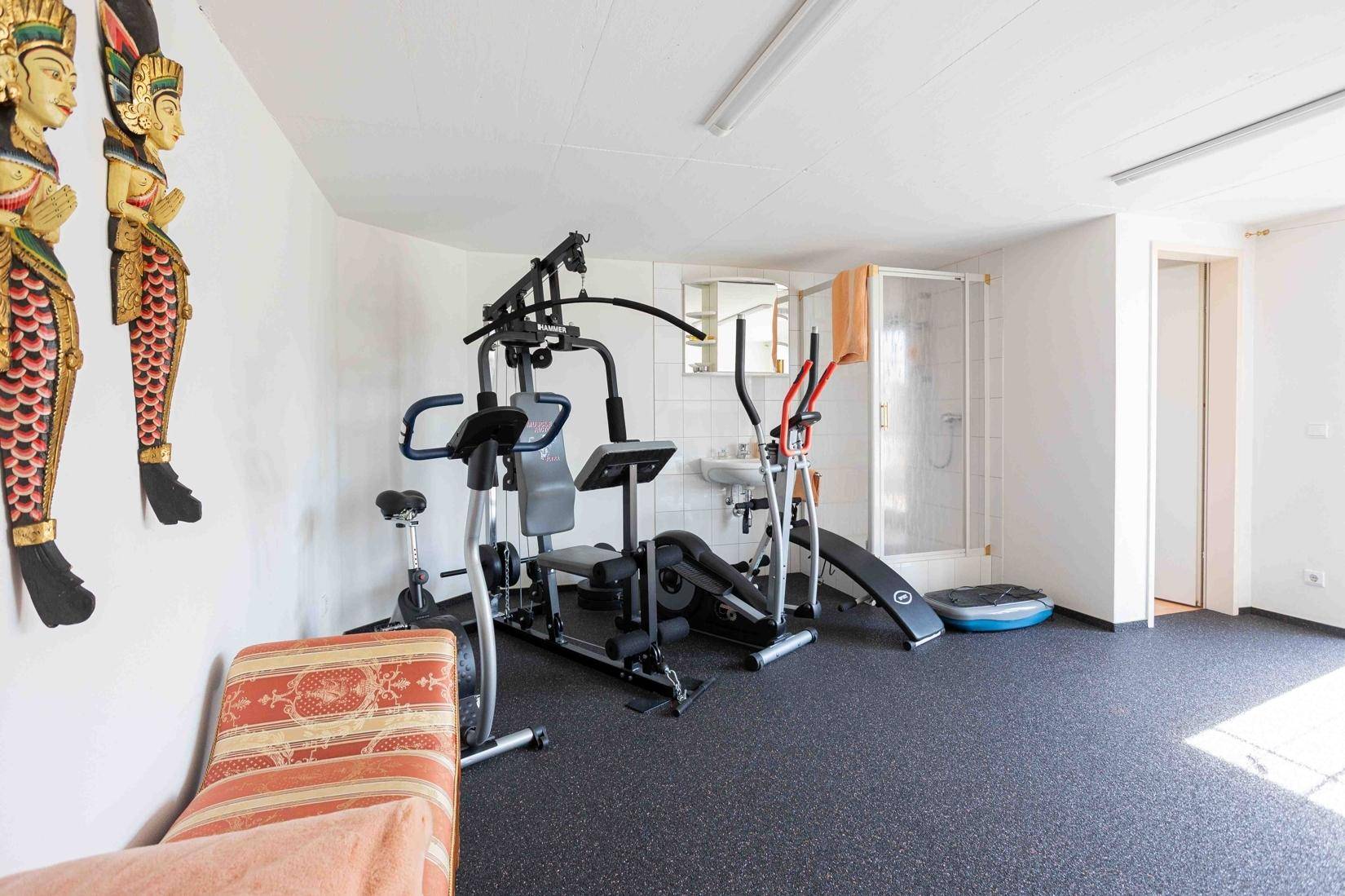 Geräumiger Fitnessraum mit verschiedenen Trainingsgeräten und Duschbereich.