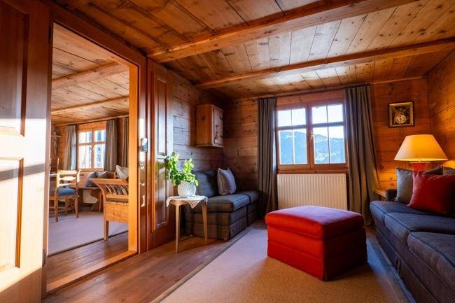 Helles Wohnzimmer mit Holzwänden, Holzbalkendecke und Zugang zum Essbereich.