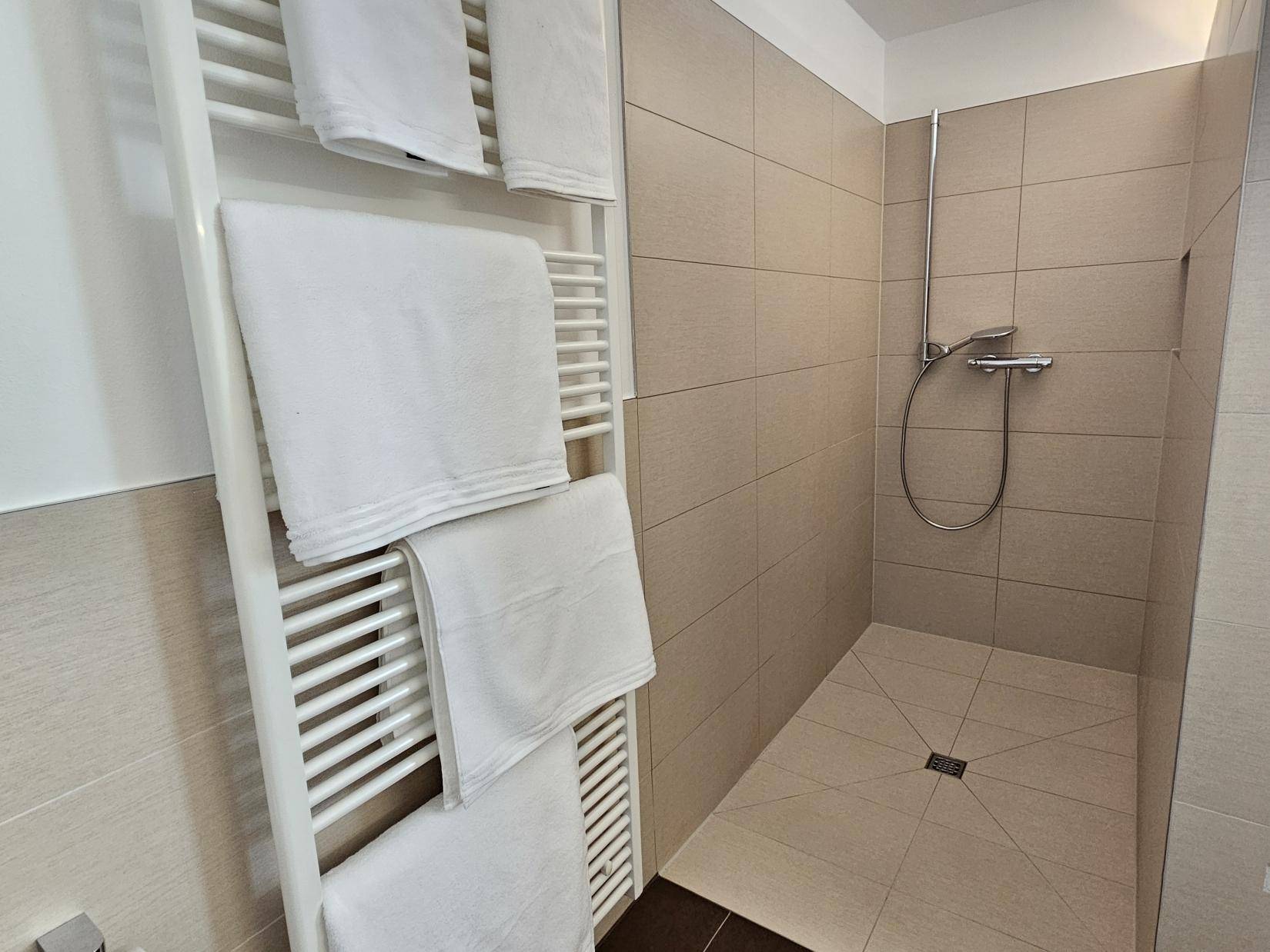 Ebenerdige Dusche mit beigefarbenen Fliesen und beheiztem Handtuchhalter.