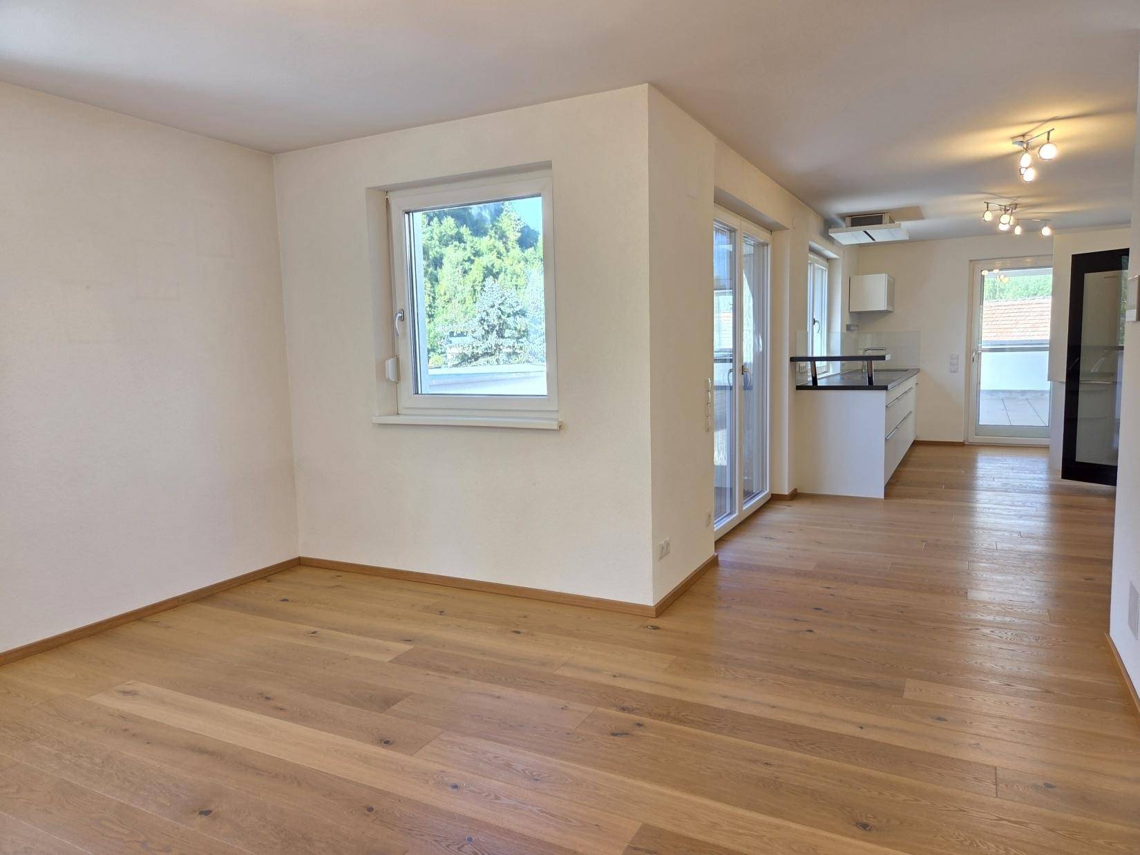 Offener Wohnbereich mit Eichenparkett, großem Fenster und Blick auf die moderne Küche mit Terrassenzugang.