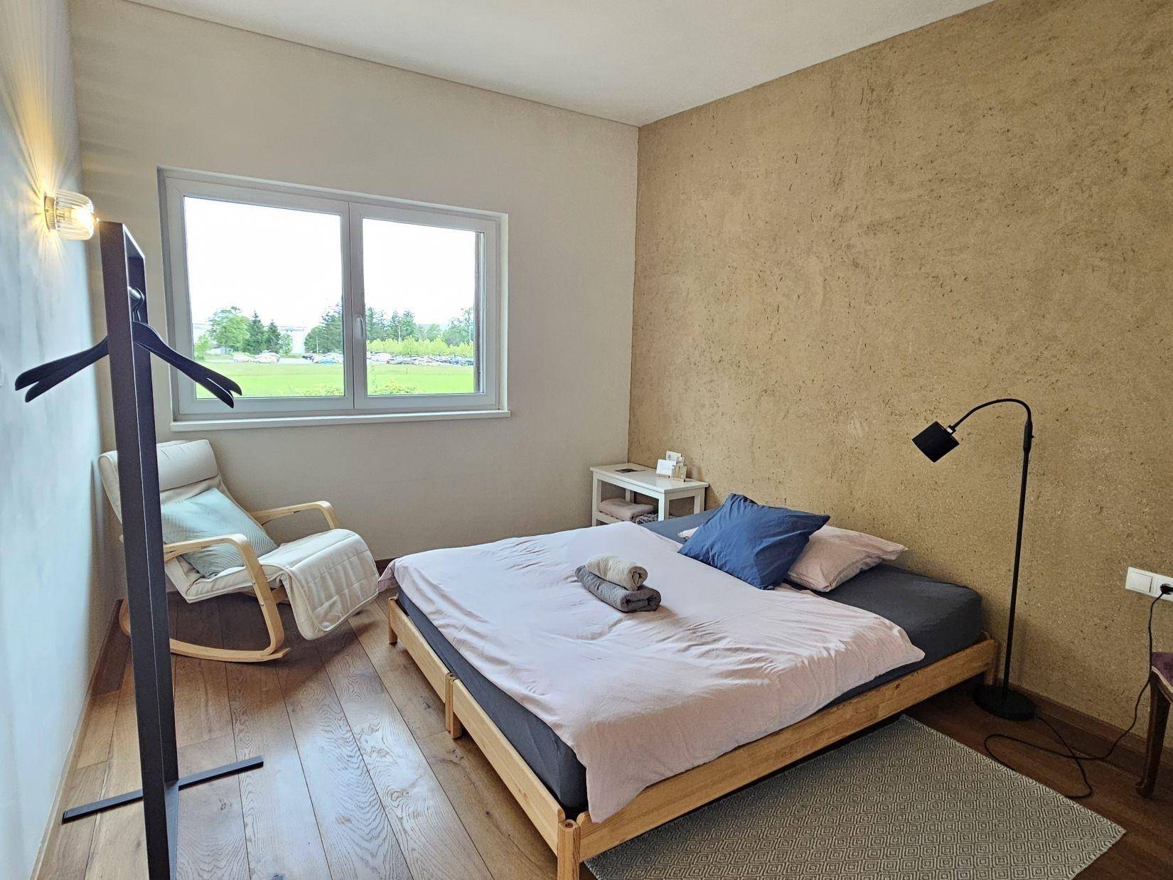 Helles Schlafzimmer mit Holzbett und Fenster, das einen weiten Blick in die Landschaft bietet.