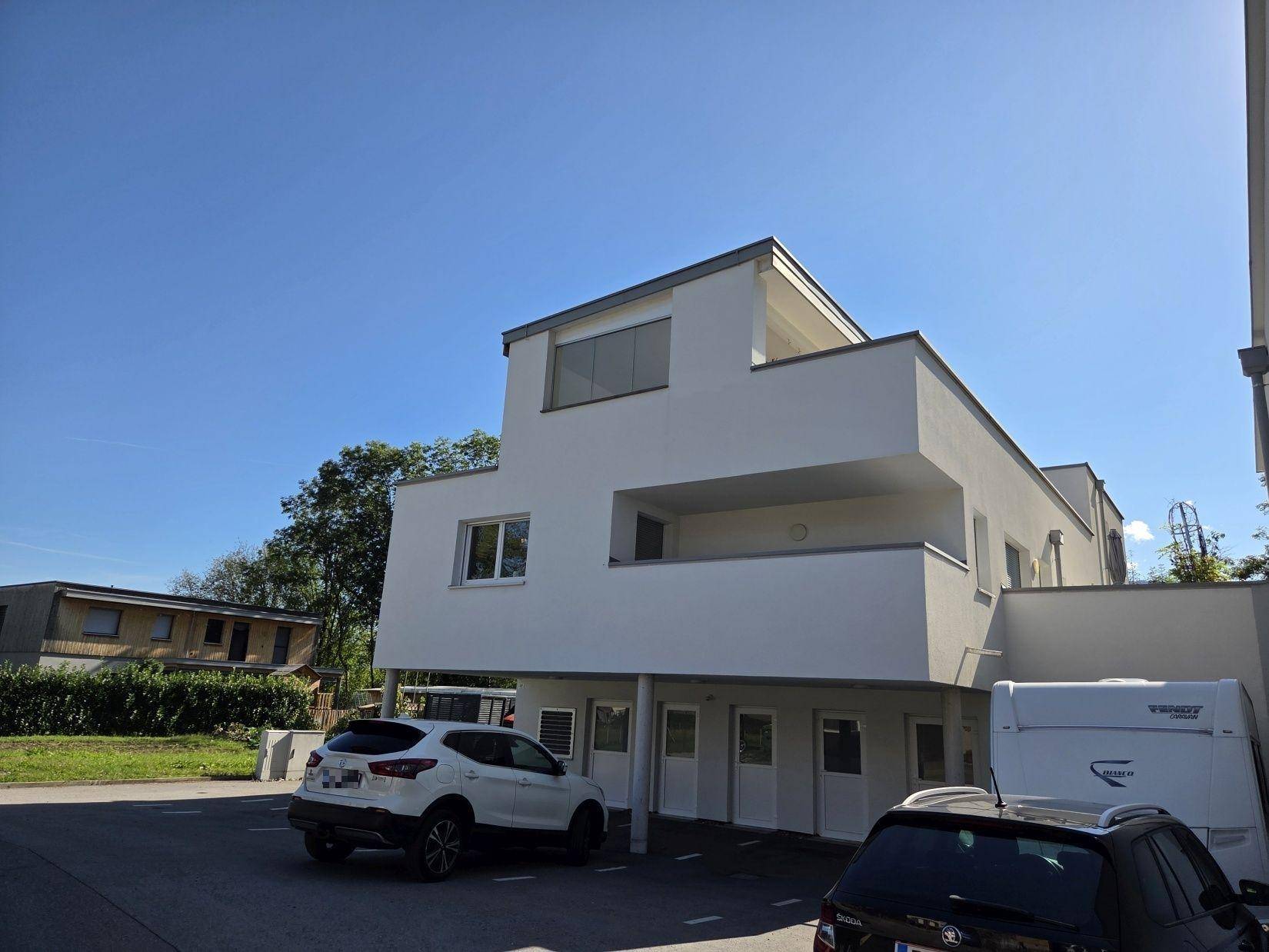 Ansicht des modernen Neubaus mit weißer Fassade und ausreichend Parkmöglichkeiten im Freien.