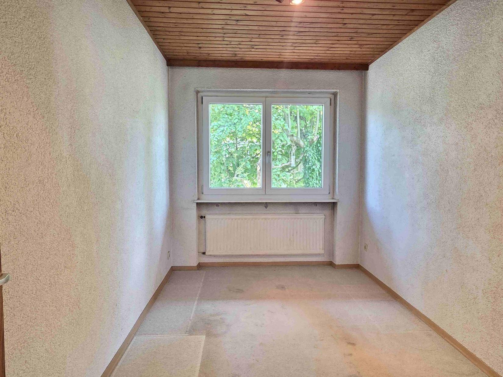Kleines Schlafzimmer mit Teppichboden, Holzdecke und Fenster mit Blick ins Grüne.