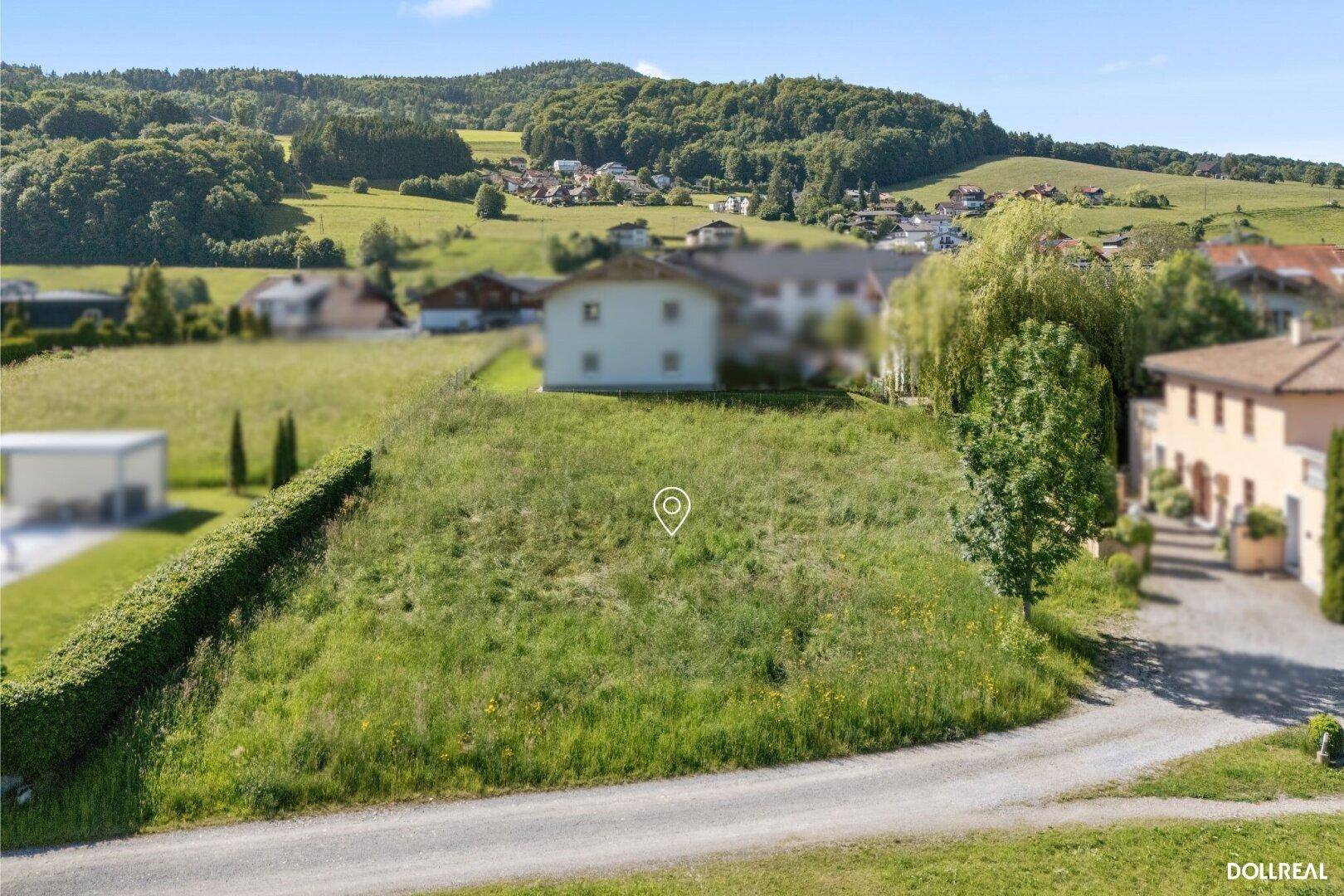 Grünes Baugrundstück mit Hecke und Blick auf die umliegende Hügellandschaft und Wohnhäuser.