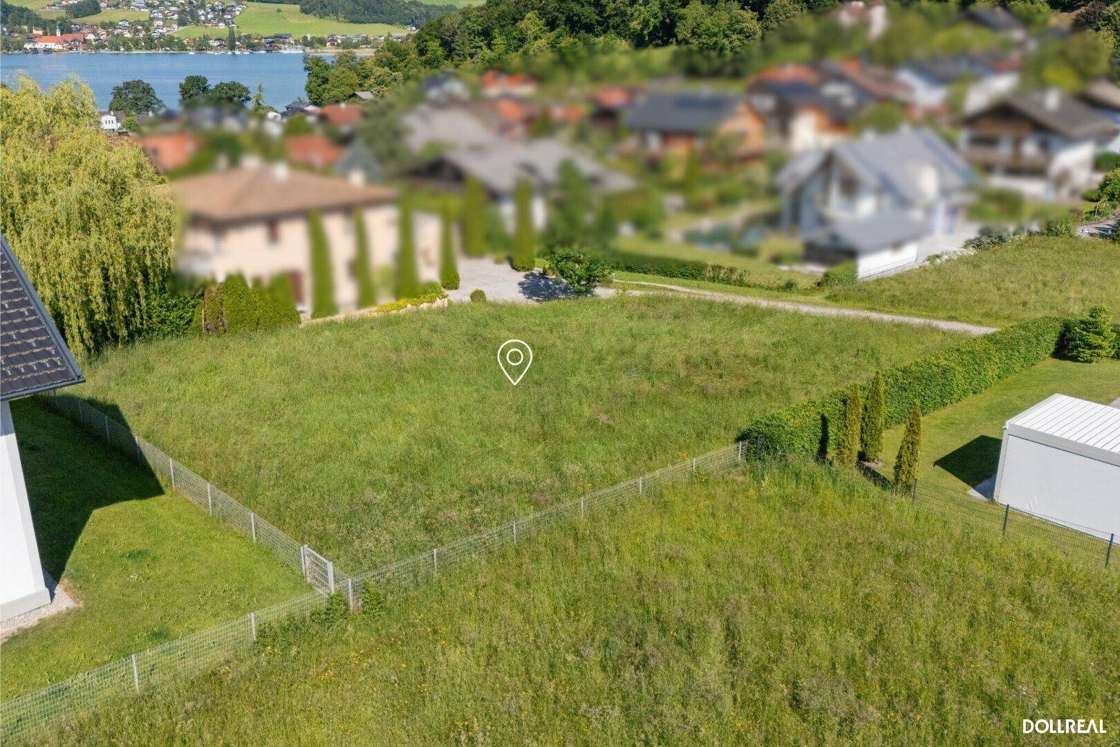 Weitläufiges Baugrundstück mit Zaun und Blick auf den See in der Ferne.