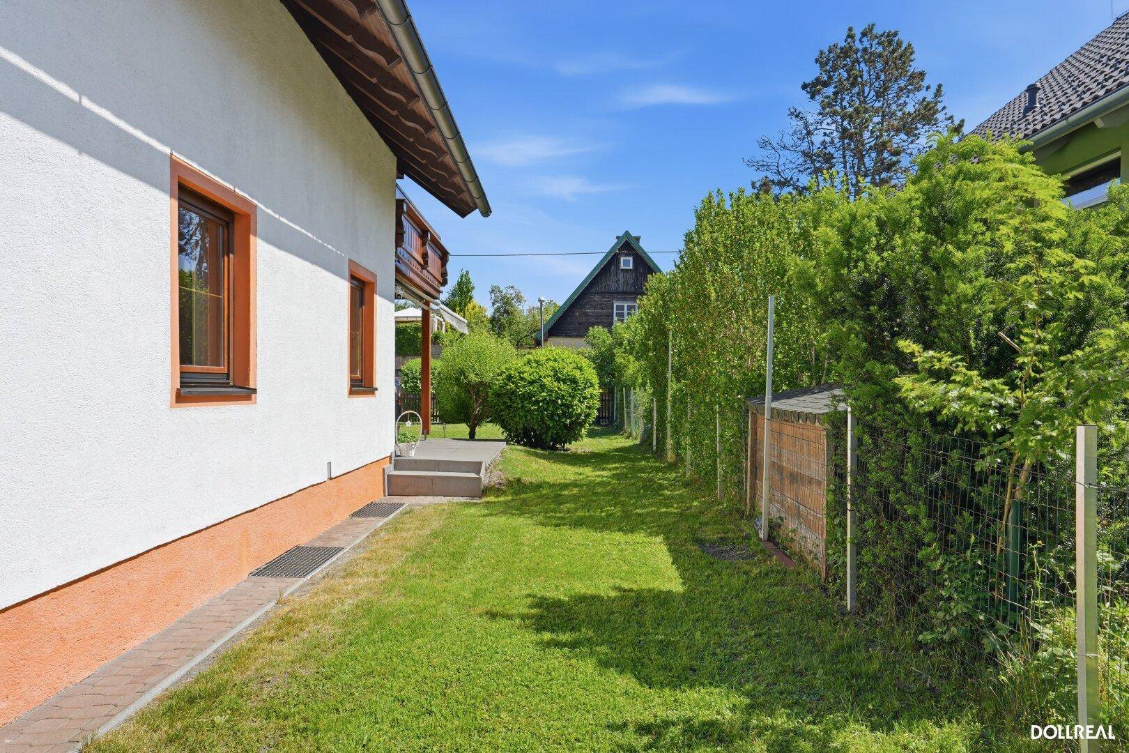 Seitlicher Zugang zum Haus mit schmalem Rasenstreifen und hohen Hecken für Privatsphäre.