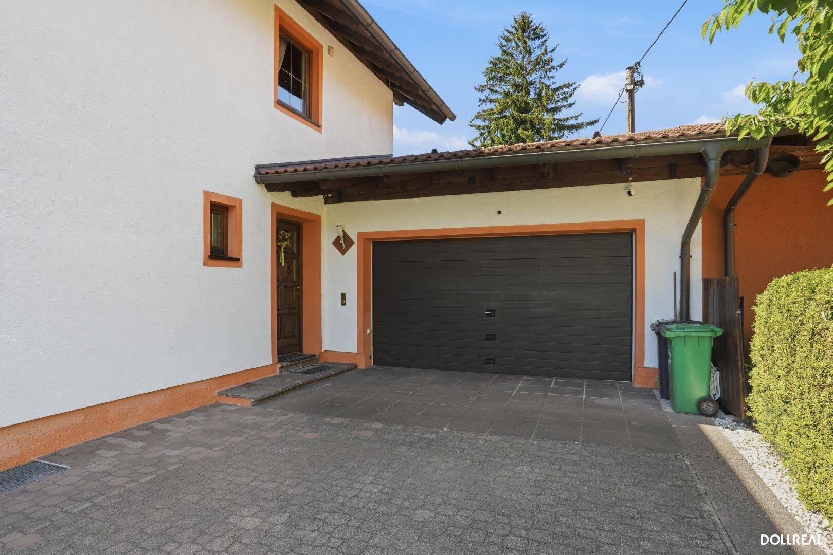 Garageneinfahrt mit dunklem Tor und direktem Zugang zum Haus unter einem Vordach.