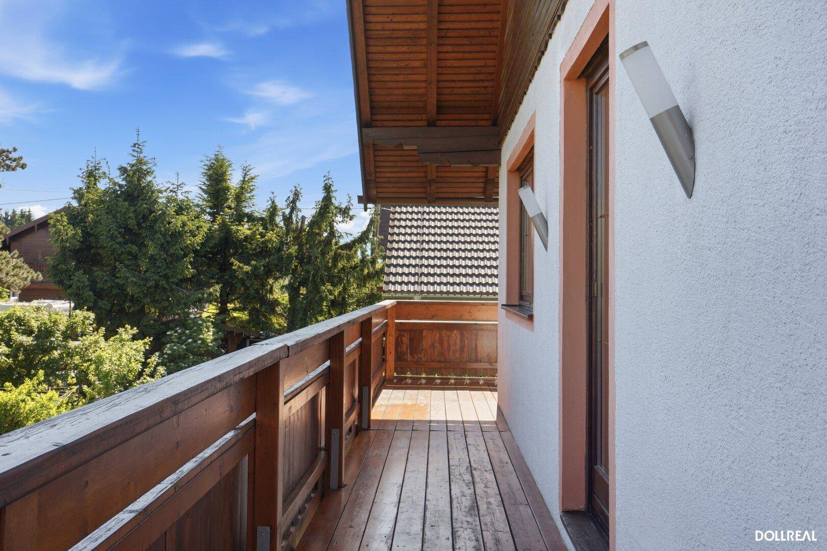 Langer Holzbalkon mit traditionellem Geländer und Blick auf die umliegende grüne Landschaft.