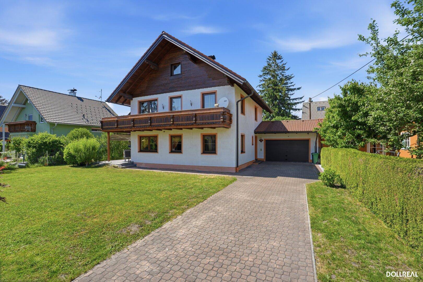 Ansicht des Einfamilienhauses mit gepflasterter Auffahrt, Rasenfläche und Holzbalkon im Obergeschoss.