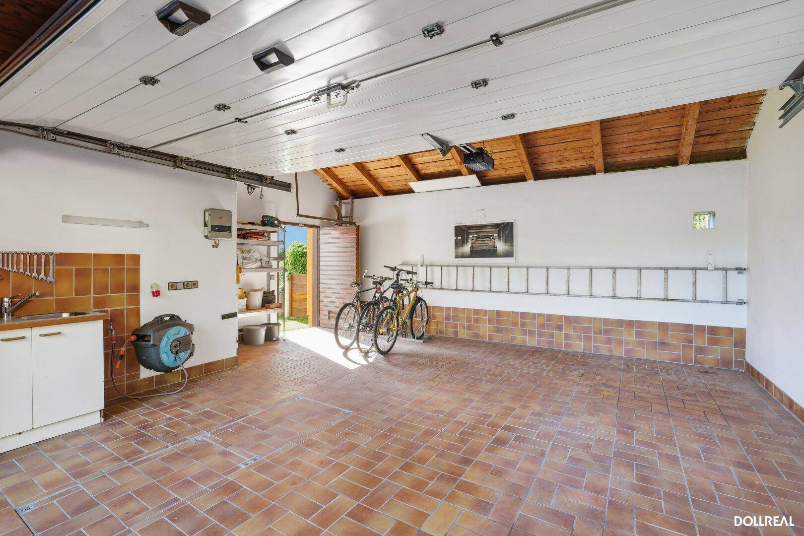 Geräumige Garage mit Fliesenboden, Werkbank und Stauraum für Fahrräder und Leitern.