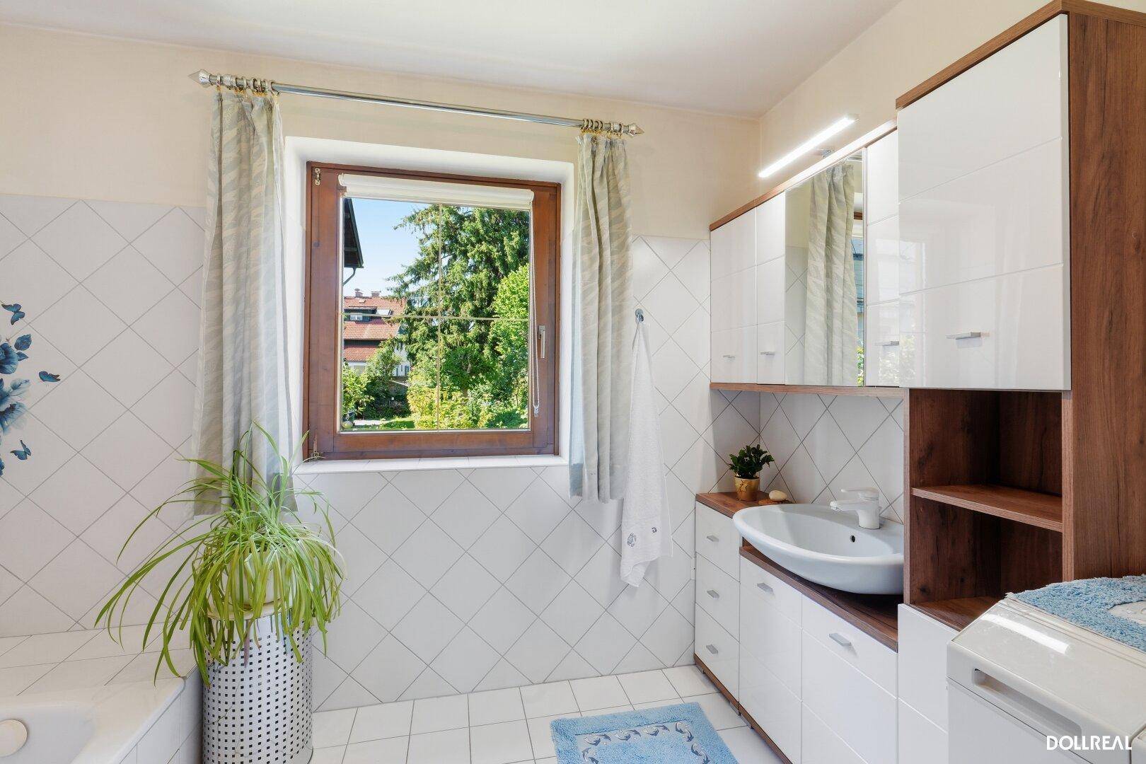 Helles Badezimmer mit weißen Fliesen, modernem Waschtisch und Fenster mit Grünblick.