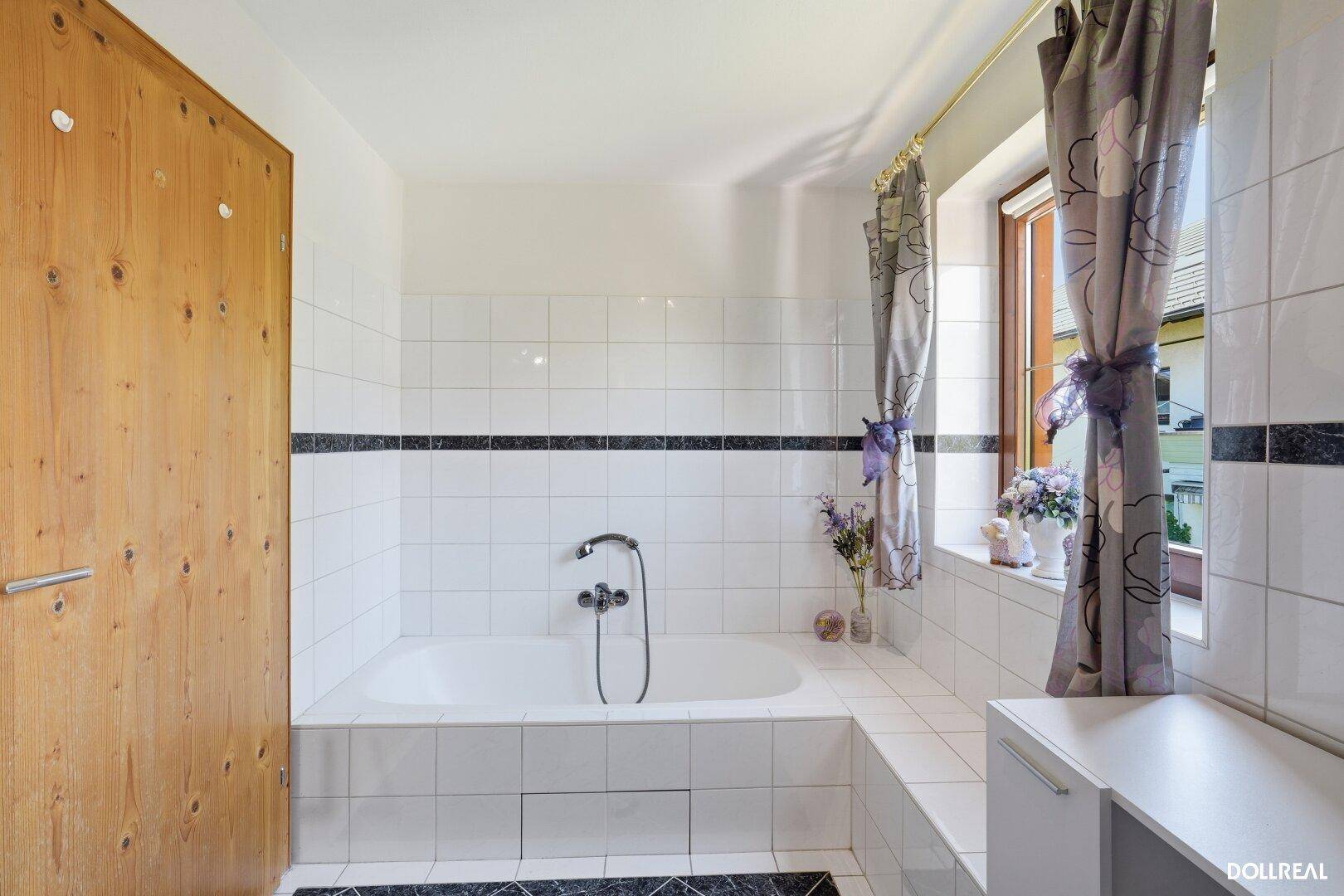 Badezimmer mit weiß gefliester Badewanne, dunklem Akzentstreifen und Fenster.