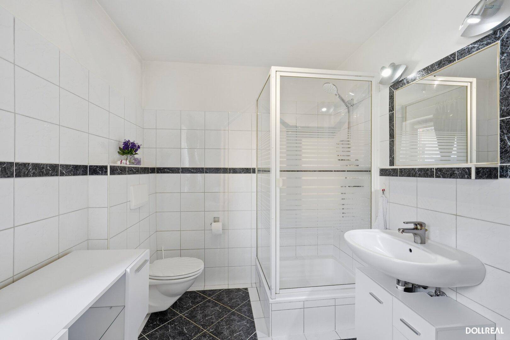 Modernes Badezimmer mit Duschkabine, Waschtisch und WC in weiß-schwarzem Design.