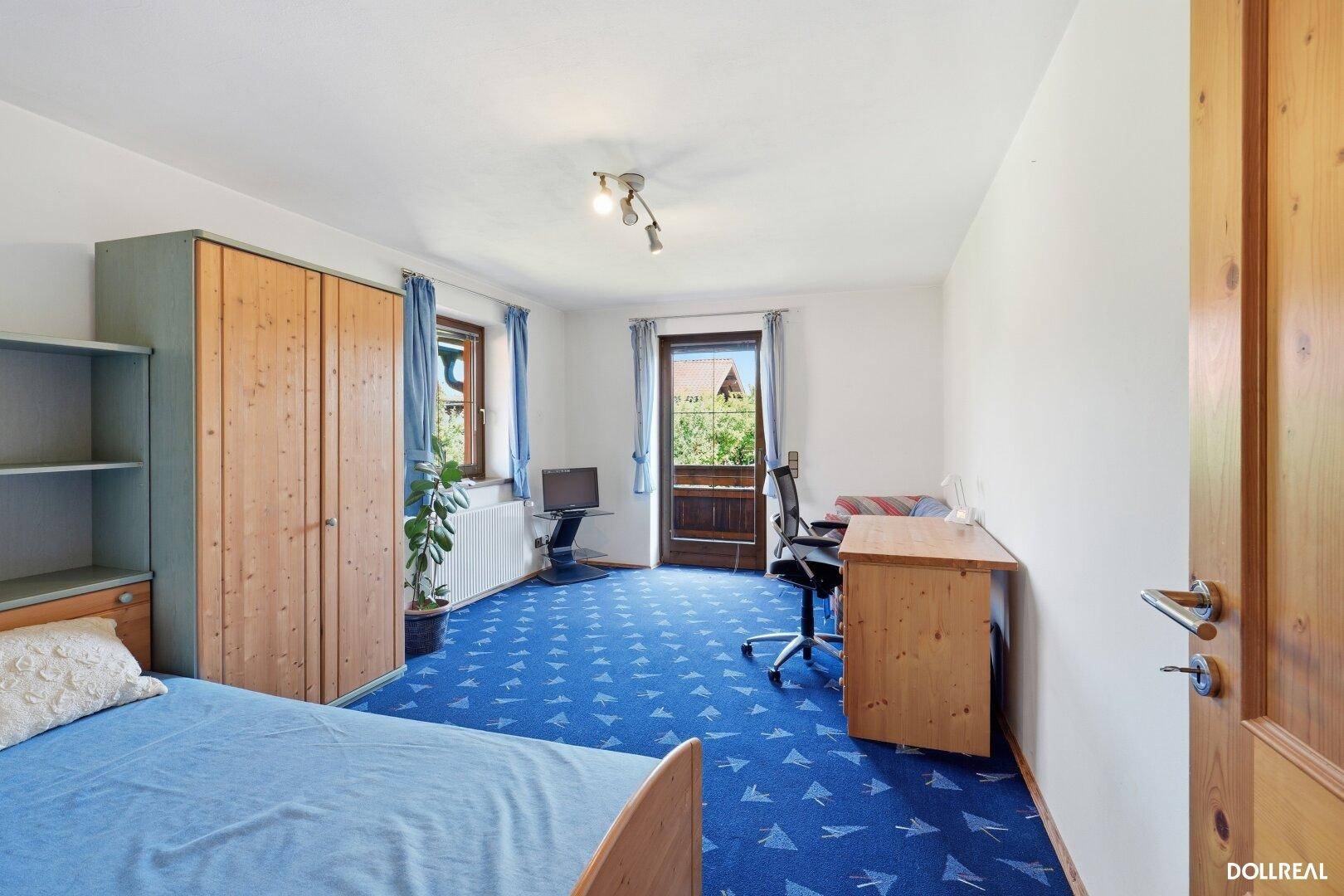 Helles Schlafzimmer mit blauem Teppichboden, Holzmöbeln und Zugang zu einem kleinen Balkon.