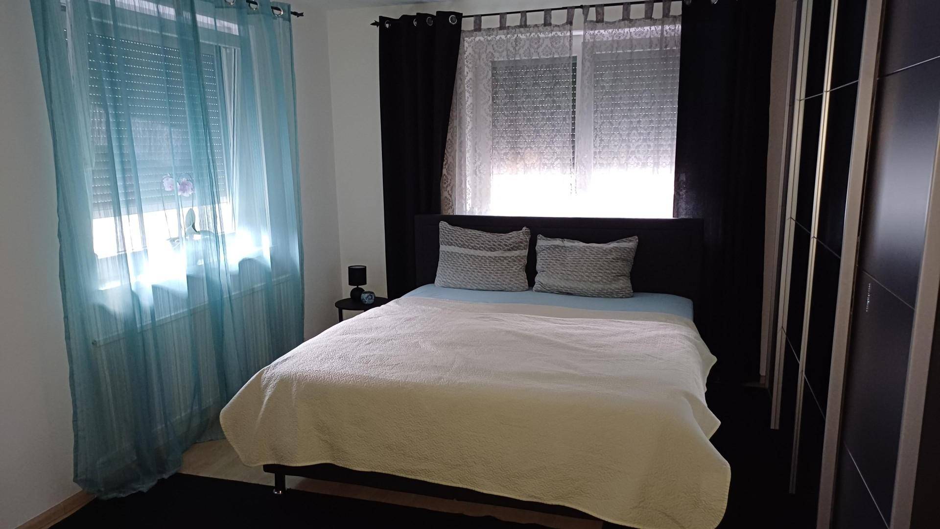 Schlafzimmer mit Doppelbett, Nachttisch und blauen Vorhängen, die eine ruhige Atmosphäre schaffen.