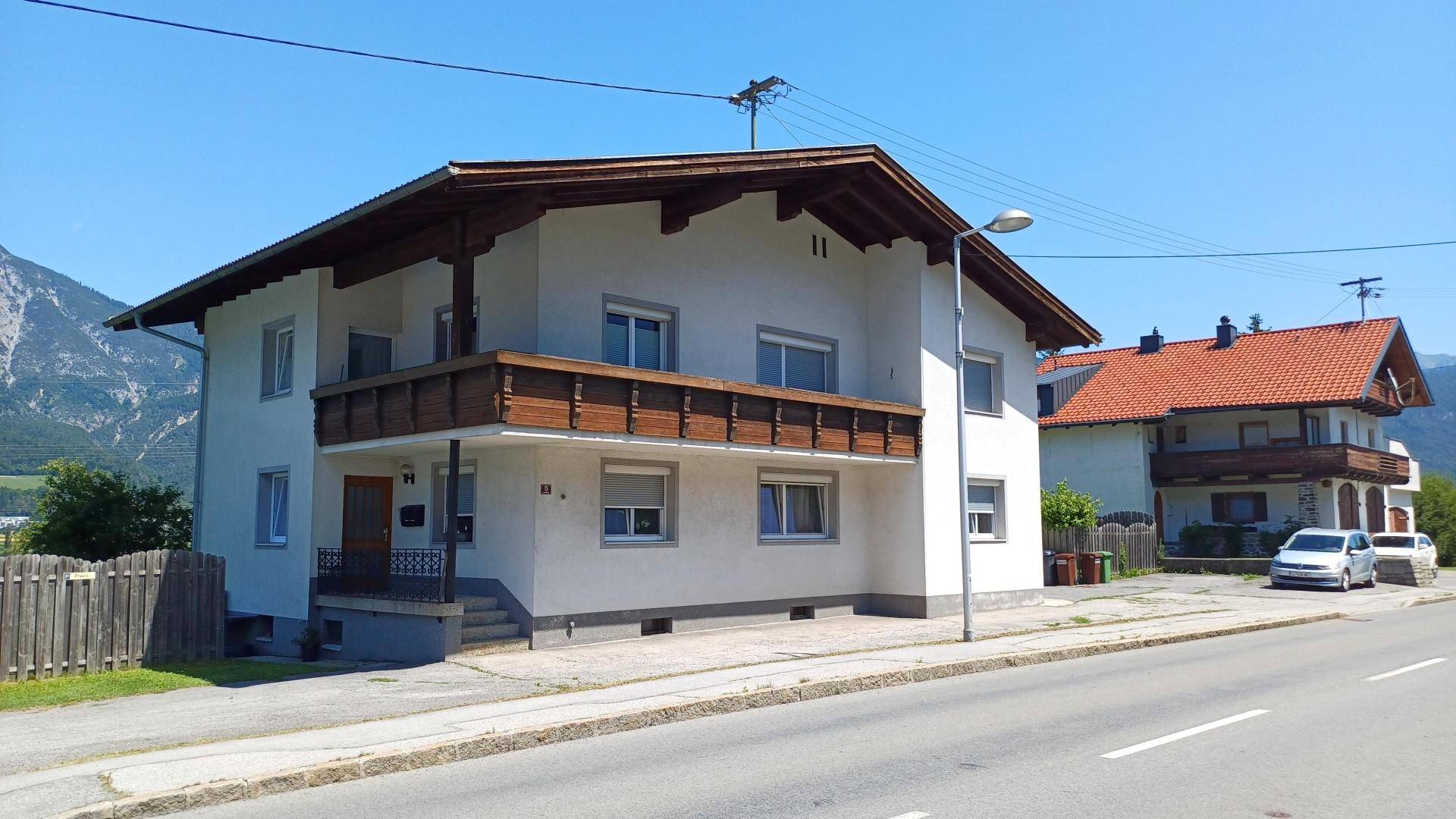 Ansicht eines Wohnhauses mit Balkon und Satteldach, umgeben von einer ländlichen Berglandschaft.