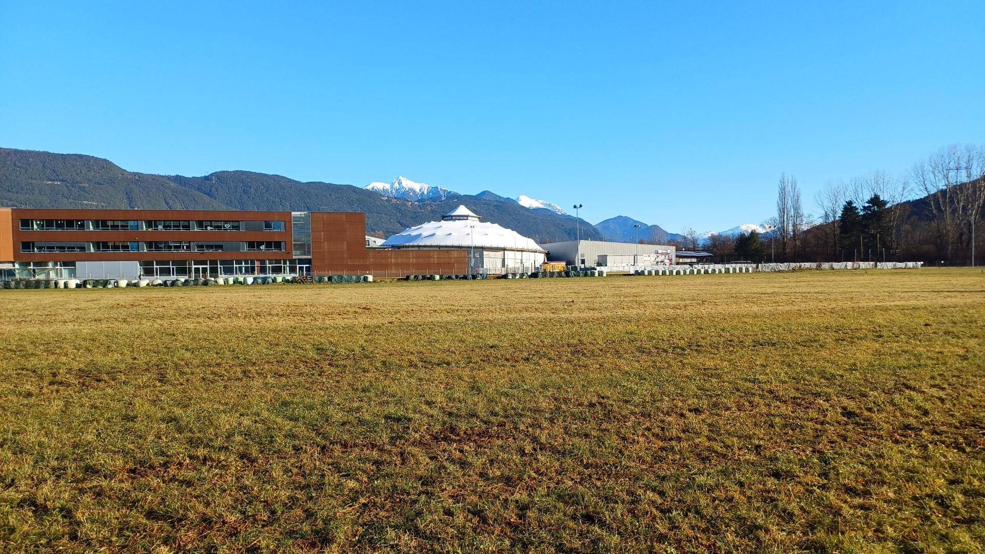 Weites Feld mit Blick auf moderne Gebäude und schneebedeckte Berge in der Ferne.