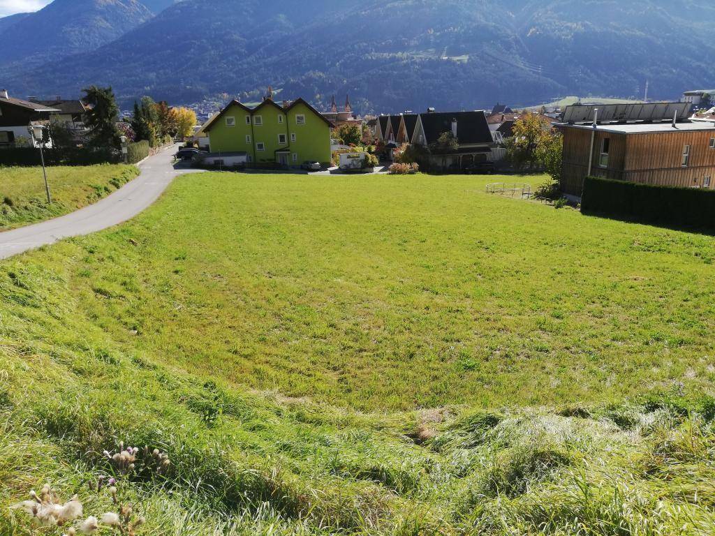 Großes grünes Feld mit kurviger Straße und Häusern im Hintergrund, umgeben von Bergen.