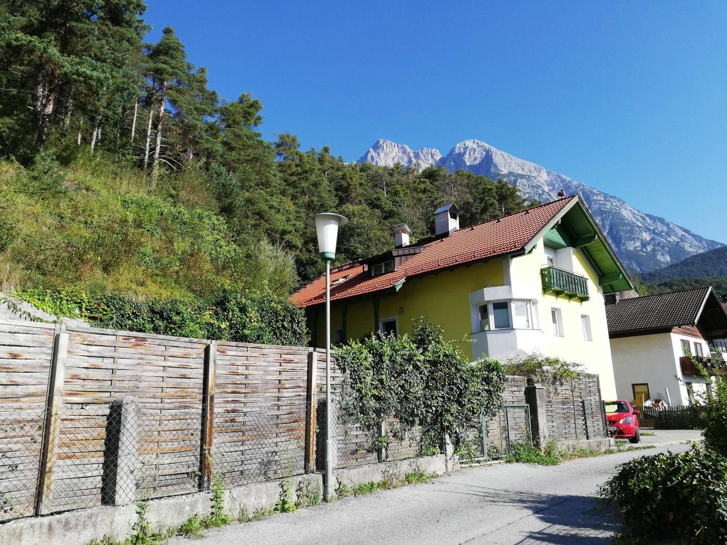 Gelbes Haus mit rotem Dach und beeindruckendem Bergblick von der Straße aus.