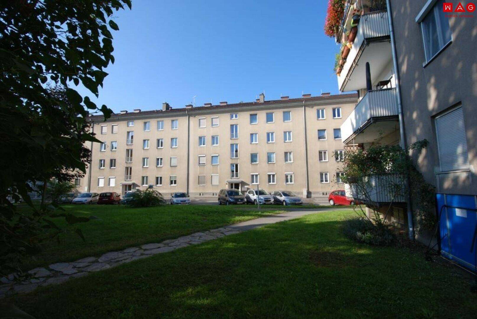 Außenansicht eines Mehrfamilienhauses mit Grünfläche und Parkplätzen im Innenhof.